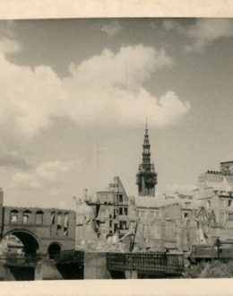 Czarno – biała powojenna fotografia przedstawiająca ruiny Gdańska. W tle widoczna wieża Ratusza oraz Kościoła Mariackiego w Gdańsku.