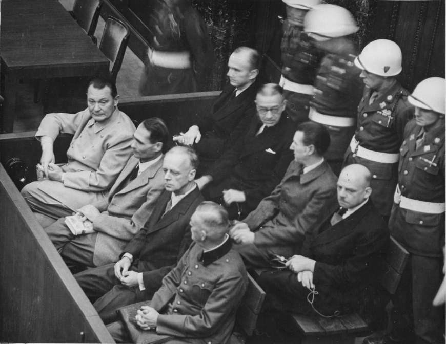 Ława oskarżonych w czasie trwania Międzynarodowego Trybunału Wojskowego w Norymberdze. Od lewej w pierwszym rzędzie: Göring, Hess, von Ribbentrop, Keitel; w drugim rzędzie: Dönitz, Raeder, Schirach, Sauckel (domena publiczna)