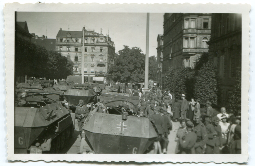 Niemiecka kolumna zmotoryzowana we francuskim mieście w trakcie działań wojennych na Zachodzie Europy w 1940 r. Na chodniku po prawej stronie widoczni są niemieccy żołnierze i ludność cywilna. Zbiory MIIWŚ w Gdańsku