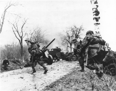 Fot. Niemieckie wojska posuwające się obok porzuconego przez Amerykanów sprzętu. 18 grudnia 1944 r. (domena publiczna)