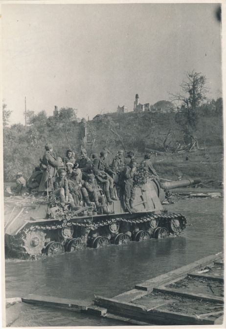 Foto 1. Oddziały Armii Czerwonej podczas walk w okolicach Grodna. Sowieccy żołnierze są przewożeni na dziale samobieżnym SU-152. W tle widoczne zniszczone zabudowania. Okupowana Polska, lato 1944 r. (autor: NN; Grodzieńskie Państwowe Muzeum Historyczno-Archeologiczne)