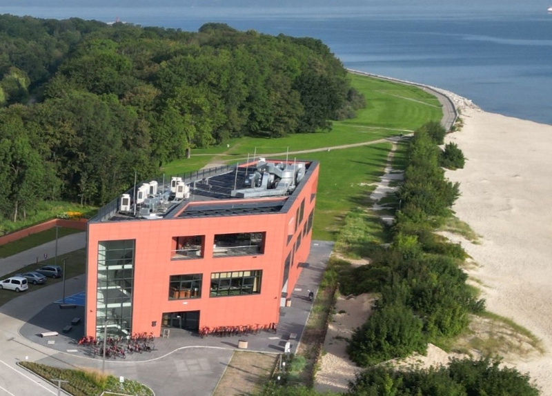 Zdjęcie budynku Centrum Obsługi Zwiedzających widziane od frontu. Piętrowy nowoczesny budynek w kolorze czerwonym. 